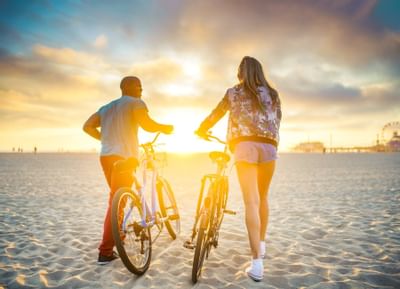 Two friends walking their bikes through the beach sand