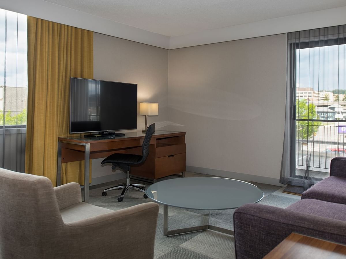 Hotel room with TV, desk, chair, couch, and table with a city view.