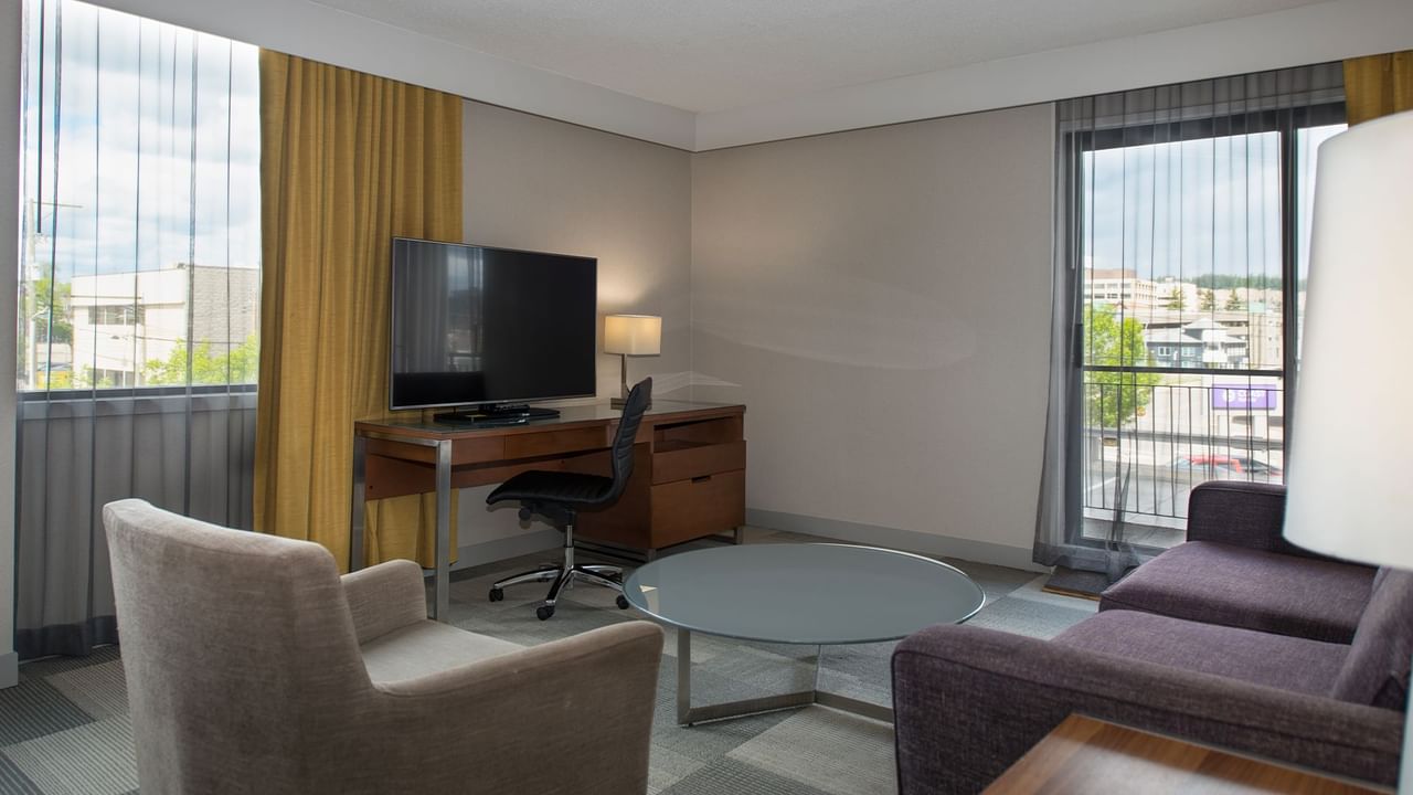 Hotel room with TV, desk, chair, couch, and table with a city view.