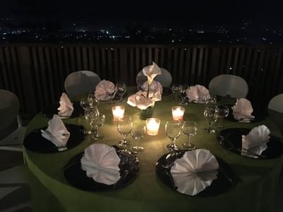 Candlelit table with folded napkins and calla lilies overlooking city lights in Olivia Room & Terrace at Hotel Montana Haiti