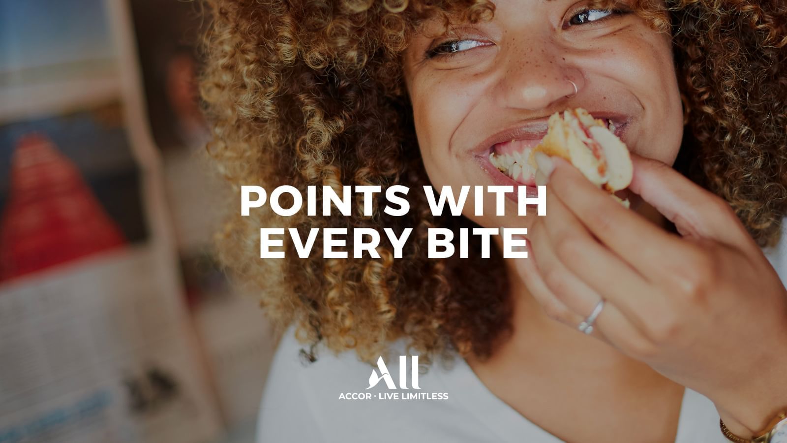 Joyful woman with curly hair takes a bite, highlighting earning Points With Every Bite at The Sebel Mandurah