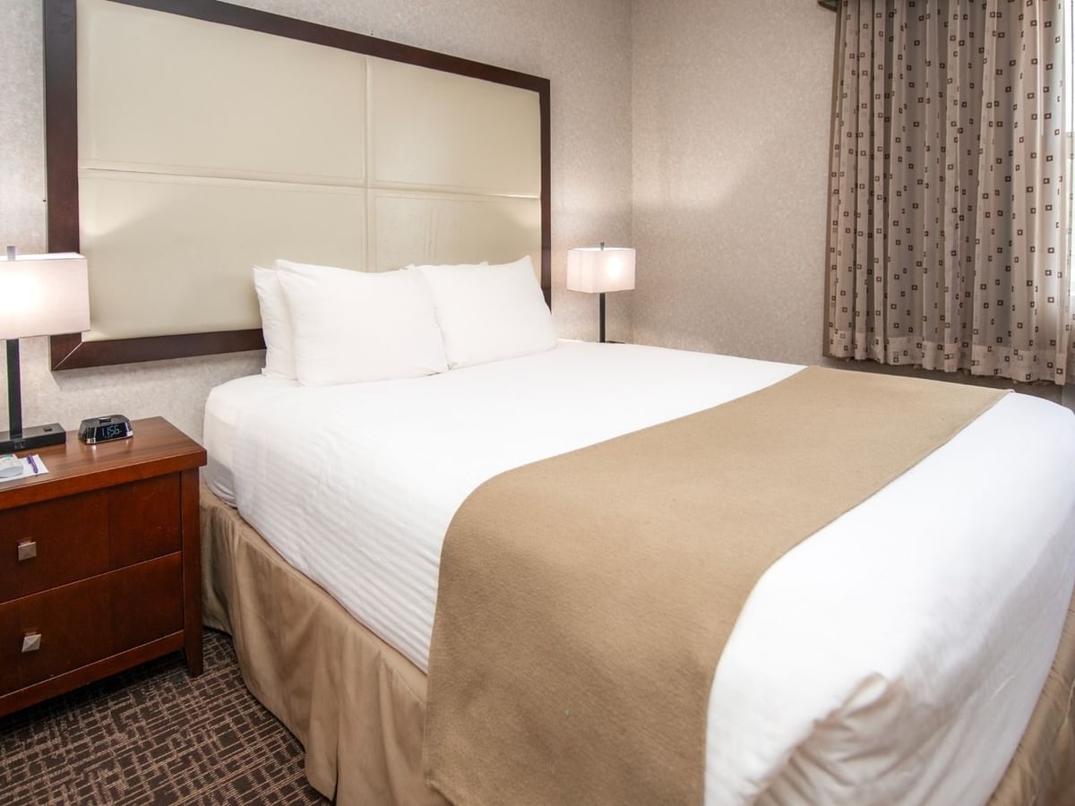 A bedroom with a large bed, two lamps, a wooden dresser, and a patterned carpet.
