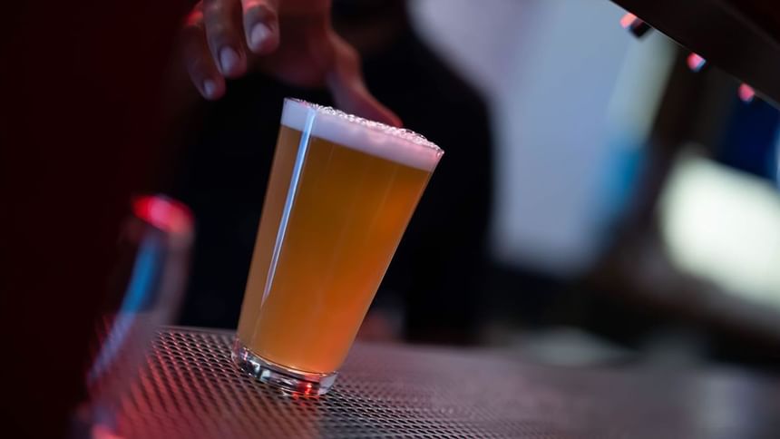 Glass of draft beer with foamy head on bar mat under dim ambient lighting in Media Sangre at Araiza Calafia
