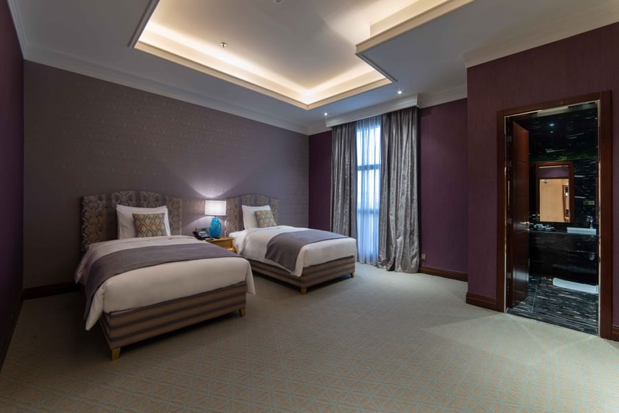 Penthouse Villa features Twin beds in a purple room by a doorway leading to a dark bathroom at Warwick Al Khobar