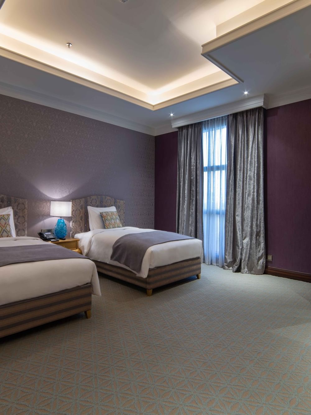 Penthouse Villa features Twin beds in a purple room by a doorway leading to a dark bathroom at Warwick Al Khobar