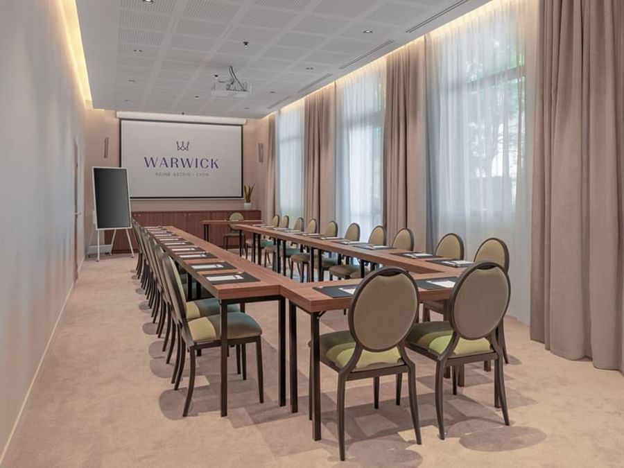 U-shaped table with green cushioned chairs and a projector screen in the Windsor meeting room at Warwick Reine Astrid - Lyon