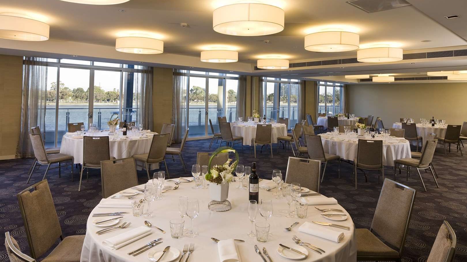 Spacious, elegant ballroom at The Sebel Mandurah set for a wedding reception with round tables and large windows