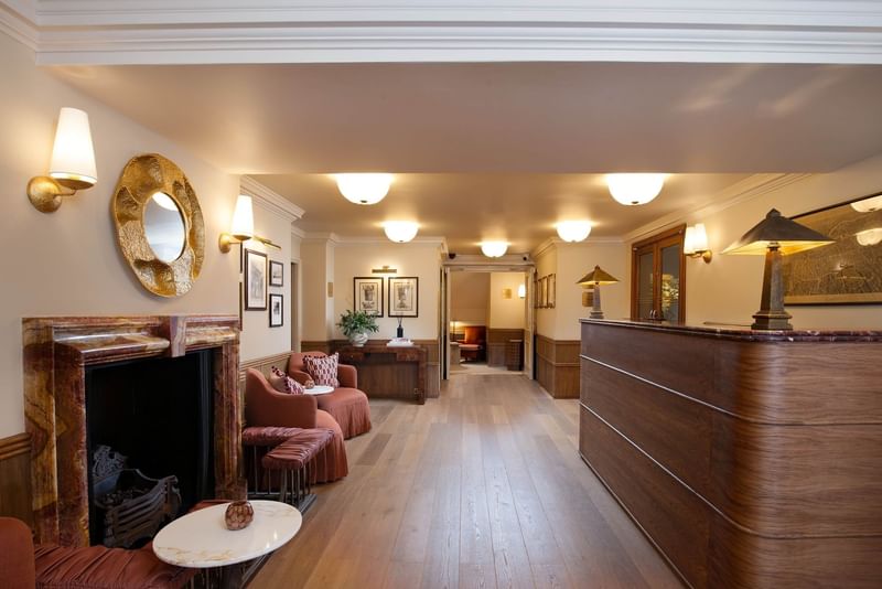 Elegant hotel lobby with marble fireplace, curved wooden reception desk, and warm lighting at The Capital Hotel, Apartments & Townhouse London Londres