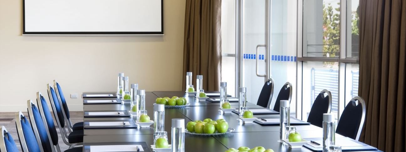 Boardroom set-up with notebooks, water glasses, and green apples in Forest Room at Novotel Sydney Olympic Park