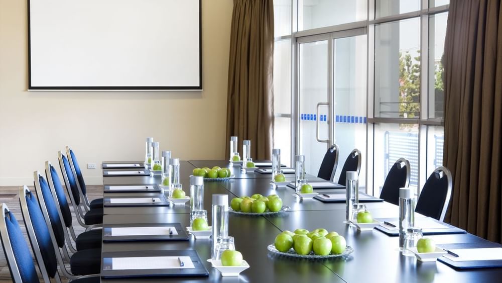 Boardroom set-up with notebooks, water glasses, and green apples in Forest Room at Novotel Sydney Olympic Park