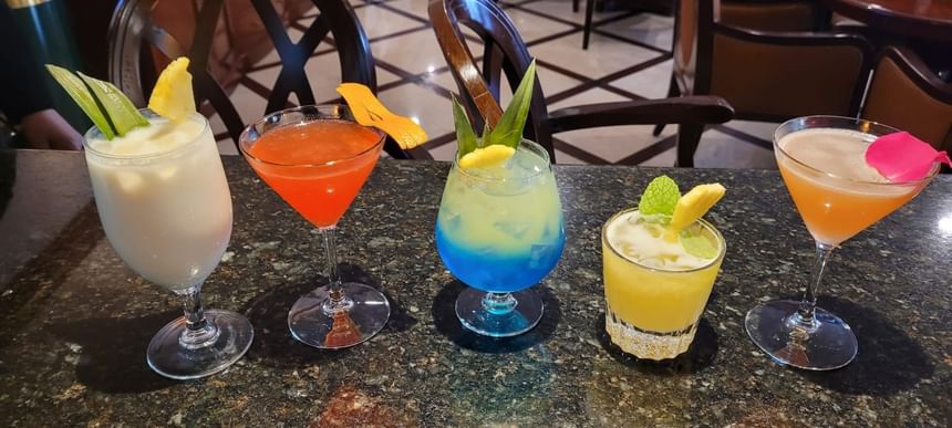 Variety of colorful cocktails on a dark countertop, featuring tropical ingredients and garnishes in The Rose Hotel