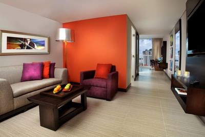 Sofa and armchair with fruit bowl on coffee table by an orange wall in Studio Suite Ocean View at Megapolis Hotel Panama