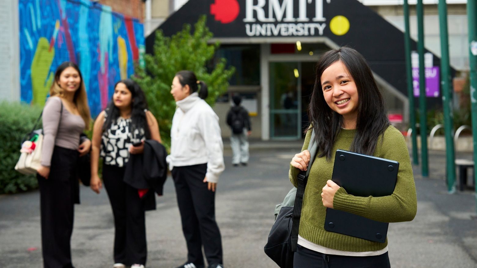 Three residents walking and talking in front of RMIT University building next to Student Living D2.
