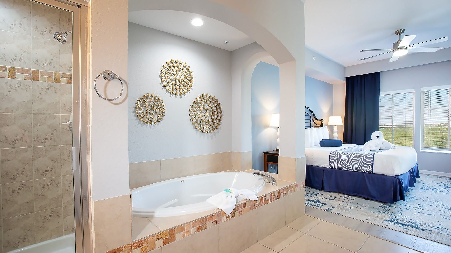 A wide view of a hotel suite with a bathtub, shower, bed, and ceiling fan.