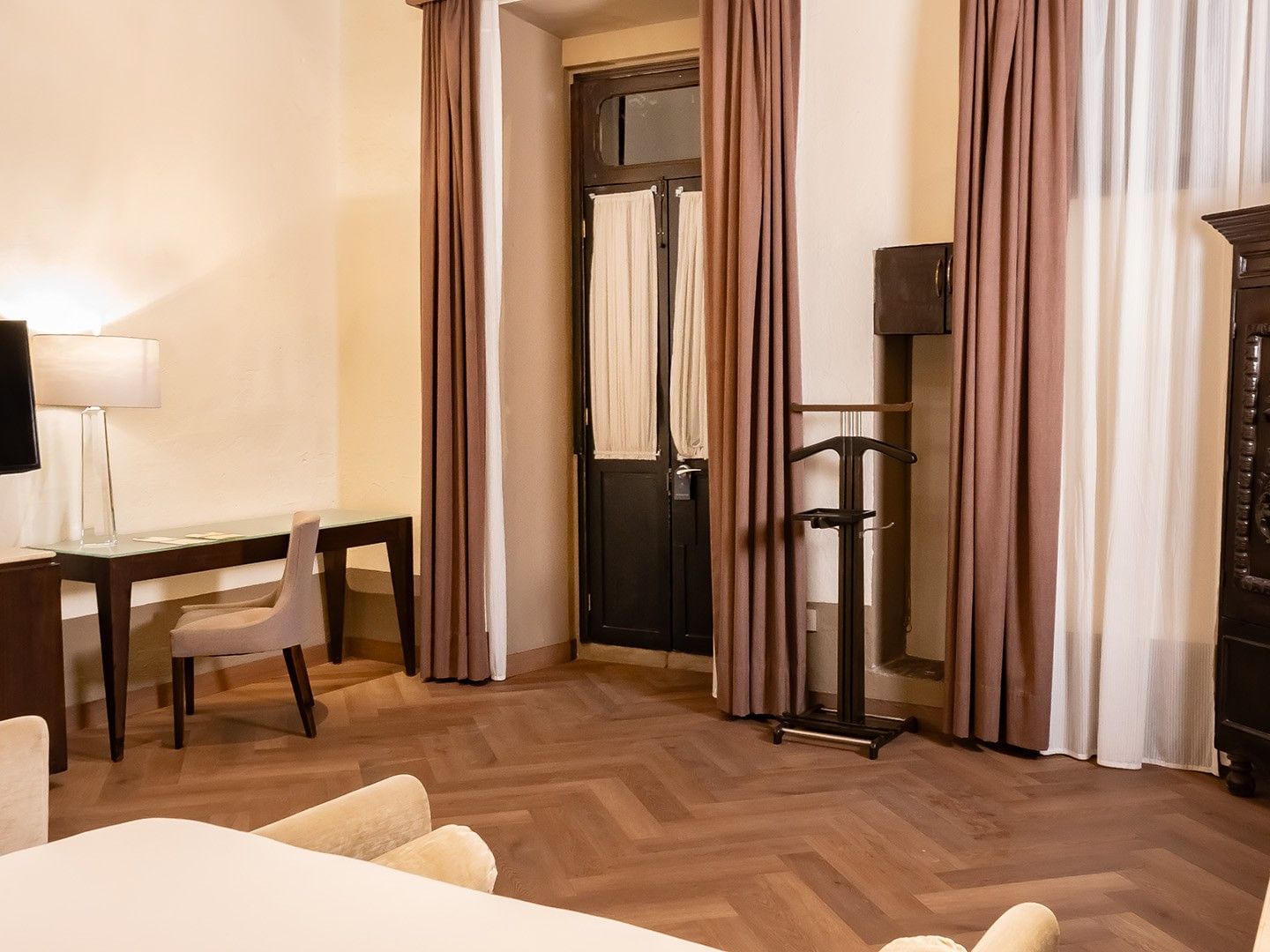 Habitación de hotel con cama, escritorio, televisor, armario, silla y suelo de madera.