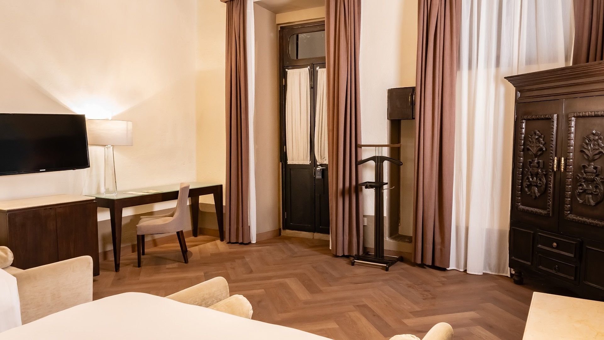 Two Double Superior room corner with a glass-top desk, brown curtains, and valet stand at Quinta Real Puebla