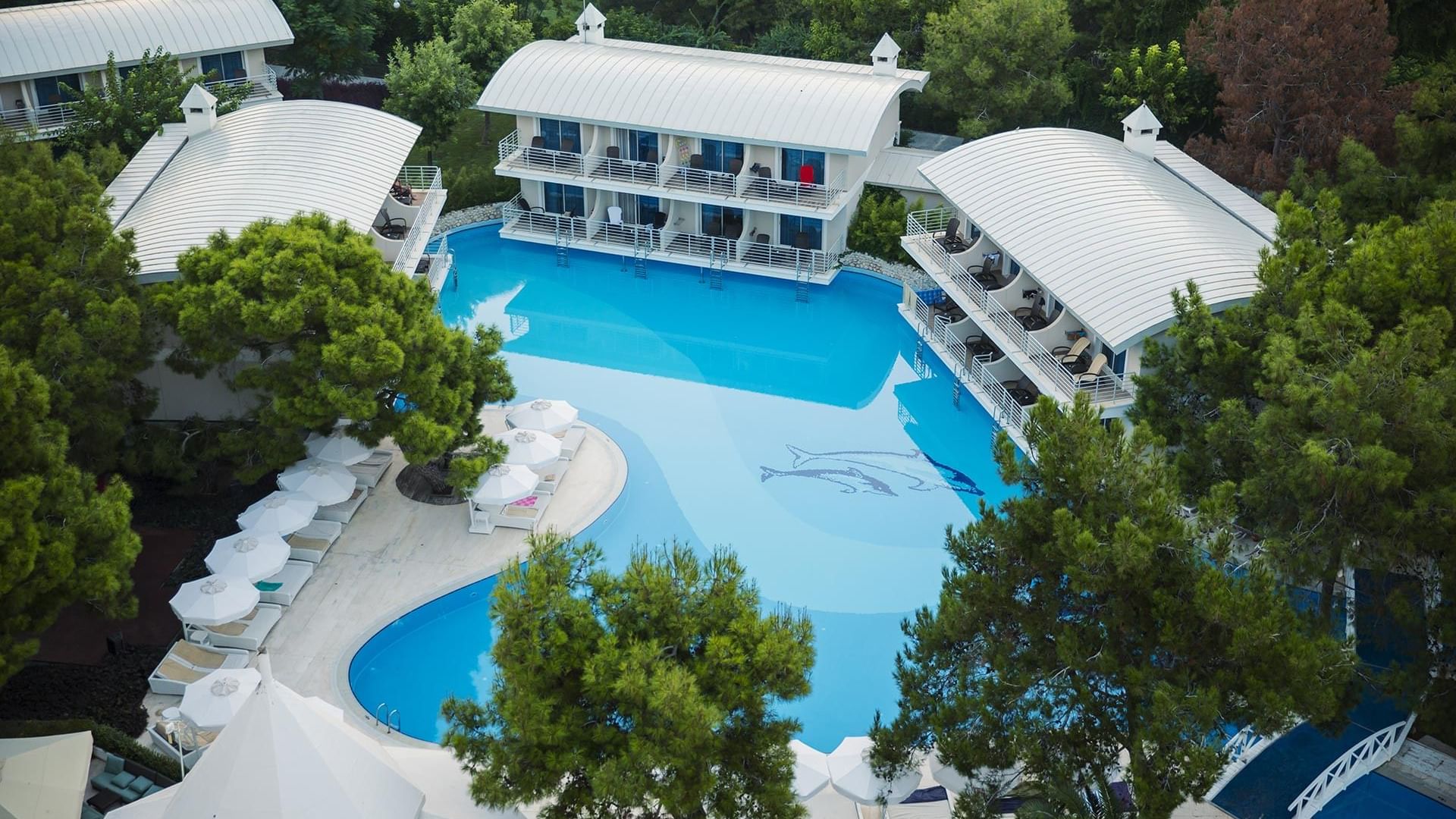 A luxurious resort surrounded by pools and white-roofed buildings nestled among green trees — an aerial view of Titanic Deluxe Lara.