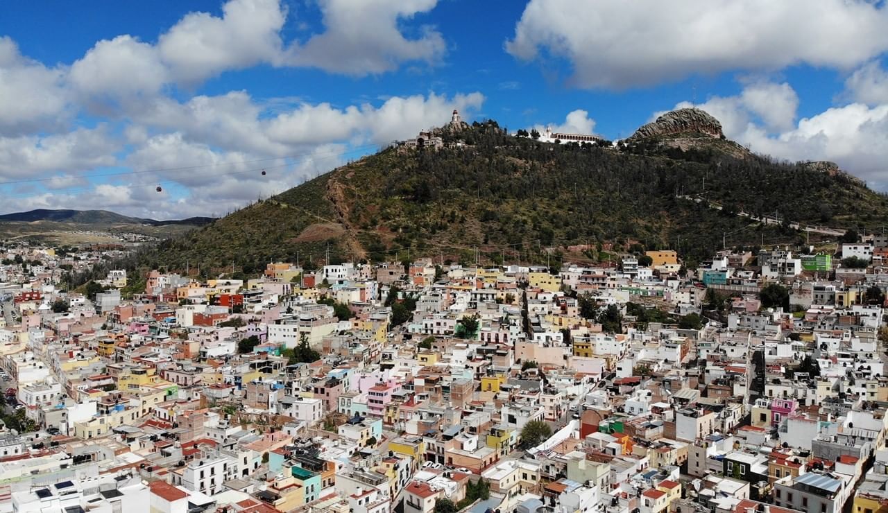 City houses by a green hill under white clouds near the cable car at the Camino Real Pedregal Mexico