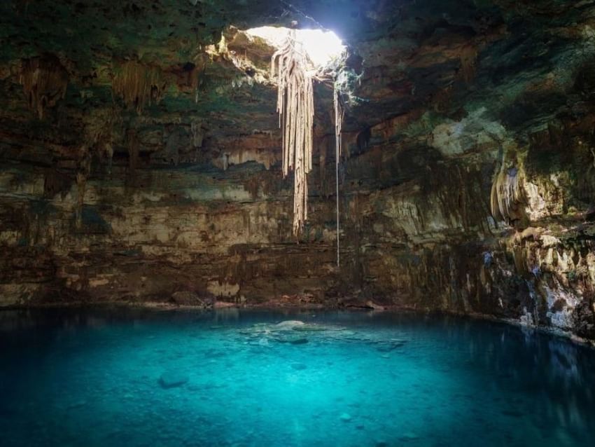Cenote subterráneo con agua azul clara y luz entrando por una cueva cerca de Camino Real