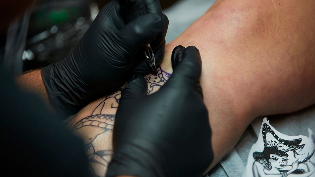 Tattoo artist wearing black gloves carefully inking an intricate design on a client's arm during Margaret River Open Studios