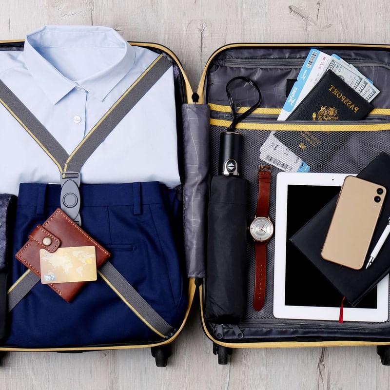 Open suitcase displays packed formal attire, passport, and travel documents at Warwick Melrose Hotel Dallas Ballroom