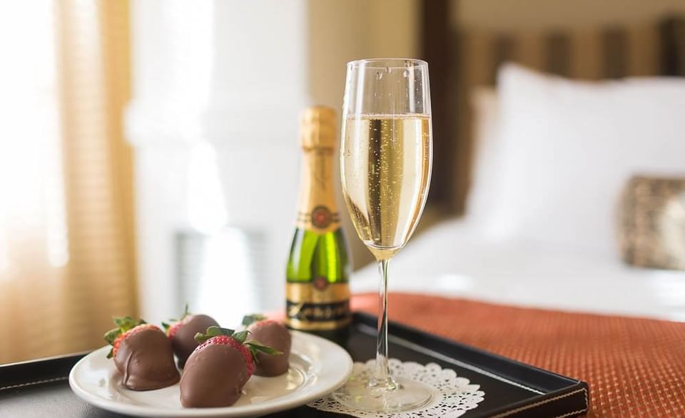 A tray with champagne, chocolate-covered strawberries, and a glass of champagne on a hotel bed at Pickwick San Francisco