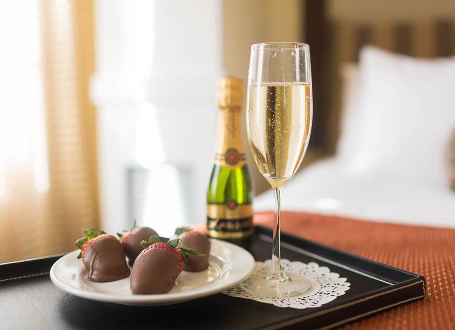 A tray with champagne, chocolate-covered strawberries, and a glass of champagne on a hotel bed at Pickwick San Francisco