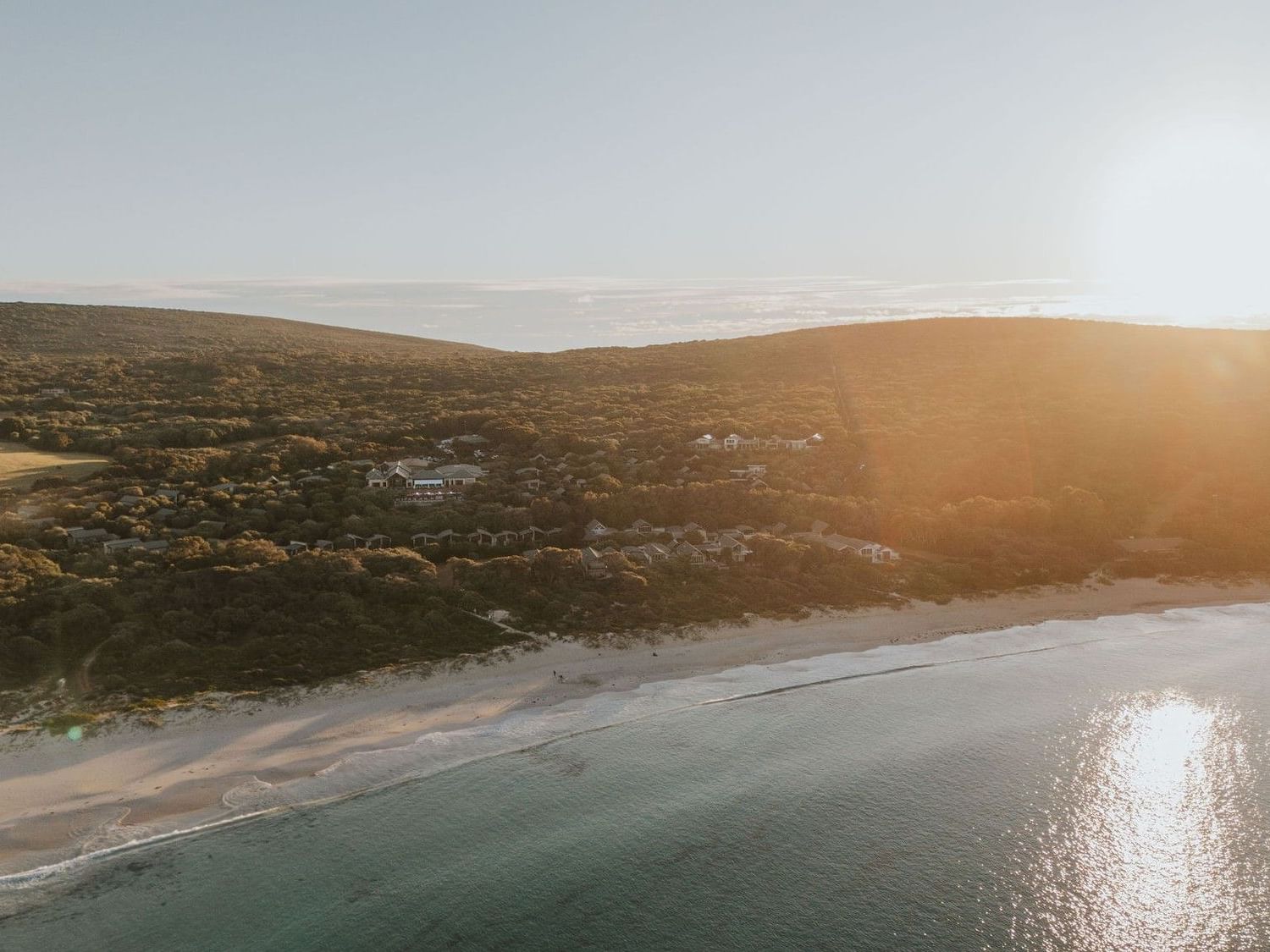Aerial view of a beach and coastal landscape with the sun setting in the sky.