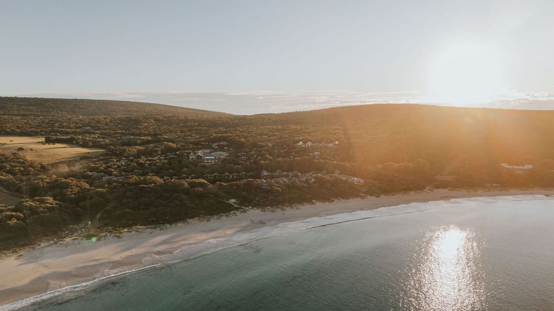 Aerial view of a beach and coastal landscape with the sun setting in the sky.