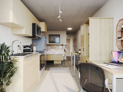 A large and modern studio apartment with full in-suite amenities, including a desk, a  desk chair, a kitchen, a dresser, a kitchen table, and a bed with under-bed storage.