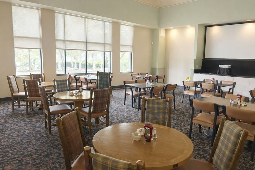 Stagedoor Restaurant room featuring wooden tables, plaid chairs, and a large projector screen at Branson Hillside Hotel