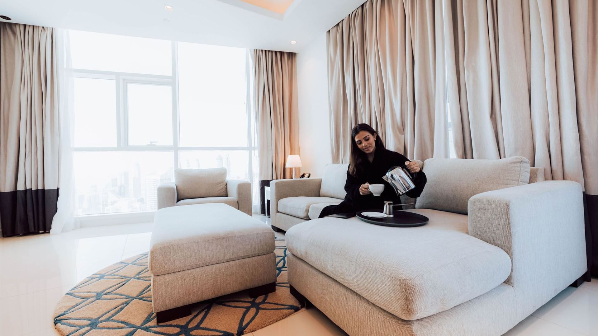 A lady pouring tea onto a cup in a hotel room at DAMAC Maison Distinction