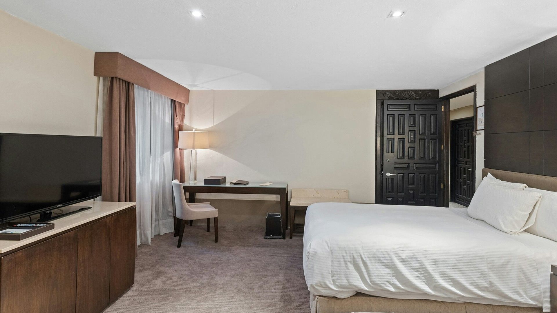 Double Grand Class Suite with a white bed, dark wood door, and a desk by a curtained window at Quinta Real Puebla