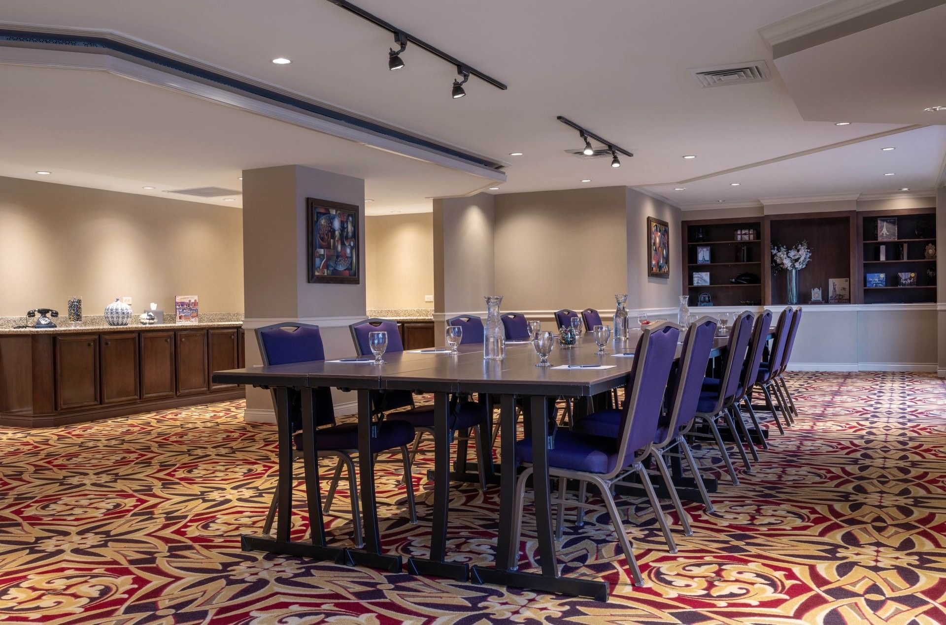 Long dark table by purple chairs under track lighting on a patterned rug in Executive Lounge at Warwick Denver