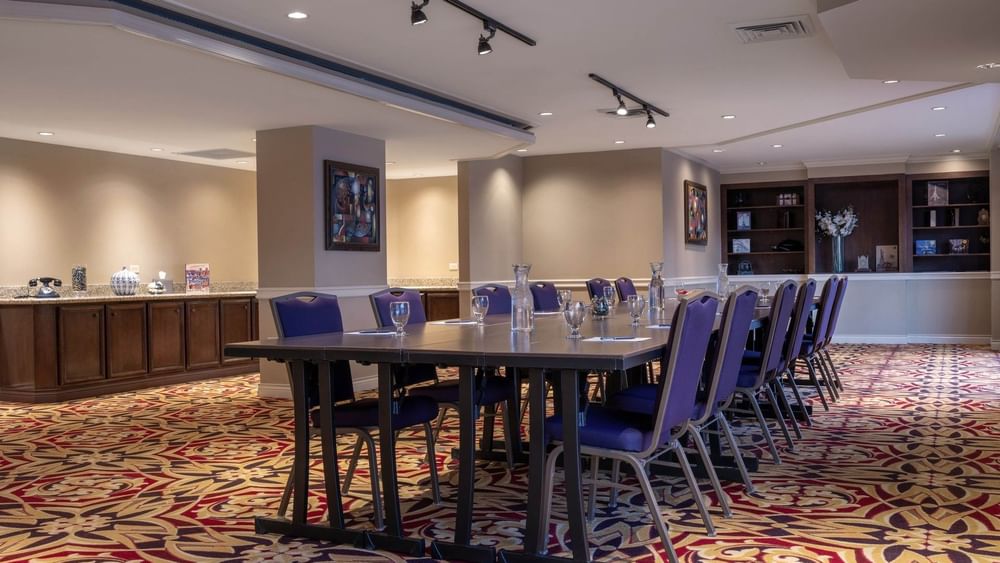 Long dark table by purple chairs under track lighting on a patterned rug in Executive Lounge at Warwick Denver