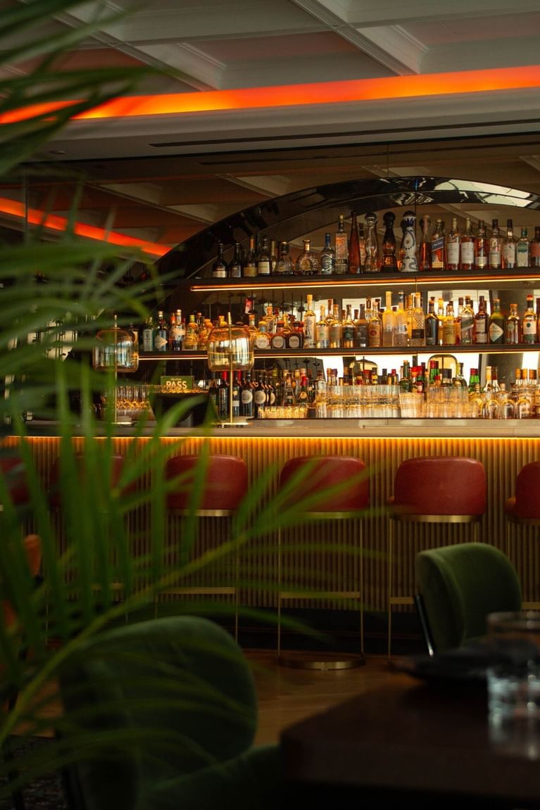 Dimly lit bar with red leather stools facing illuminated liquor shelves and dining tables at Hotel X Toronto