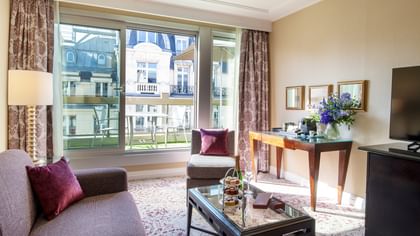 Elegant hotel room with large window, couch, coffee table, and balcony view at Warwick Champs-Elysées Paris