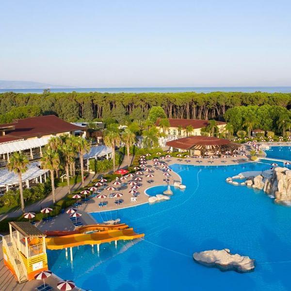 Vista aerea di un resort con piscine, scivoli acquatici, ombrelloni e edifici in un ambiente boschivo.