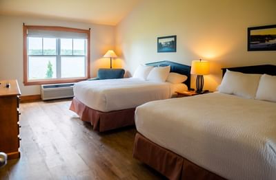 Two-Bedroom Cottage featuring two large beds by a wide window overlooking water at Rodd Brudenell River Resort