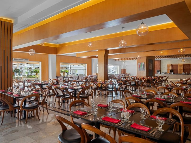 قاعة طعام كبيرة بها طاولات وكراسٍ، ومفارش حمراء، وشموع، ونوافذ كبيرة.