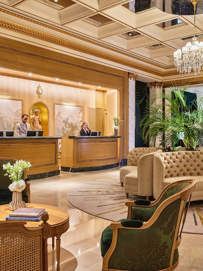Hall d'hôtel luxueux avec réception en bois doré, canapés capitonnés beiges, lustres en cristal et colonnes en marbre