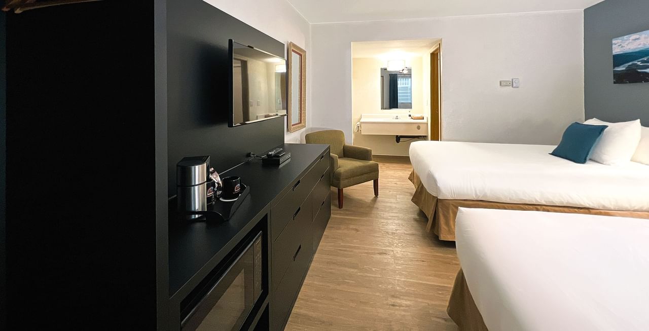 Hotel bedroom with two beds, chair, TV, microwave, coffee maker, and mirror