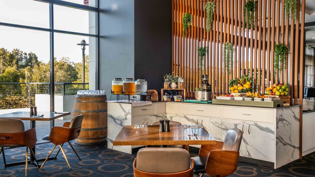 Buffet Breakfast area interior with juice dispensers, fresh fruits, and furniture with windows at Mercure Kooindah Waters