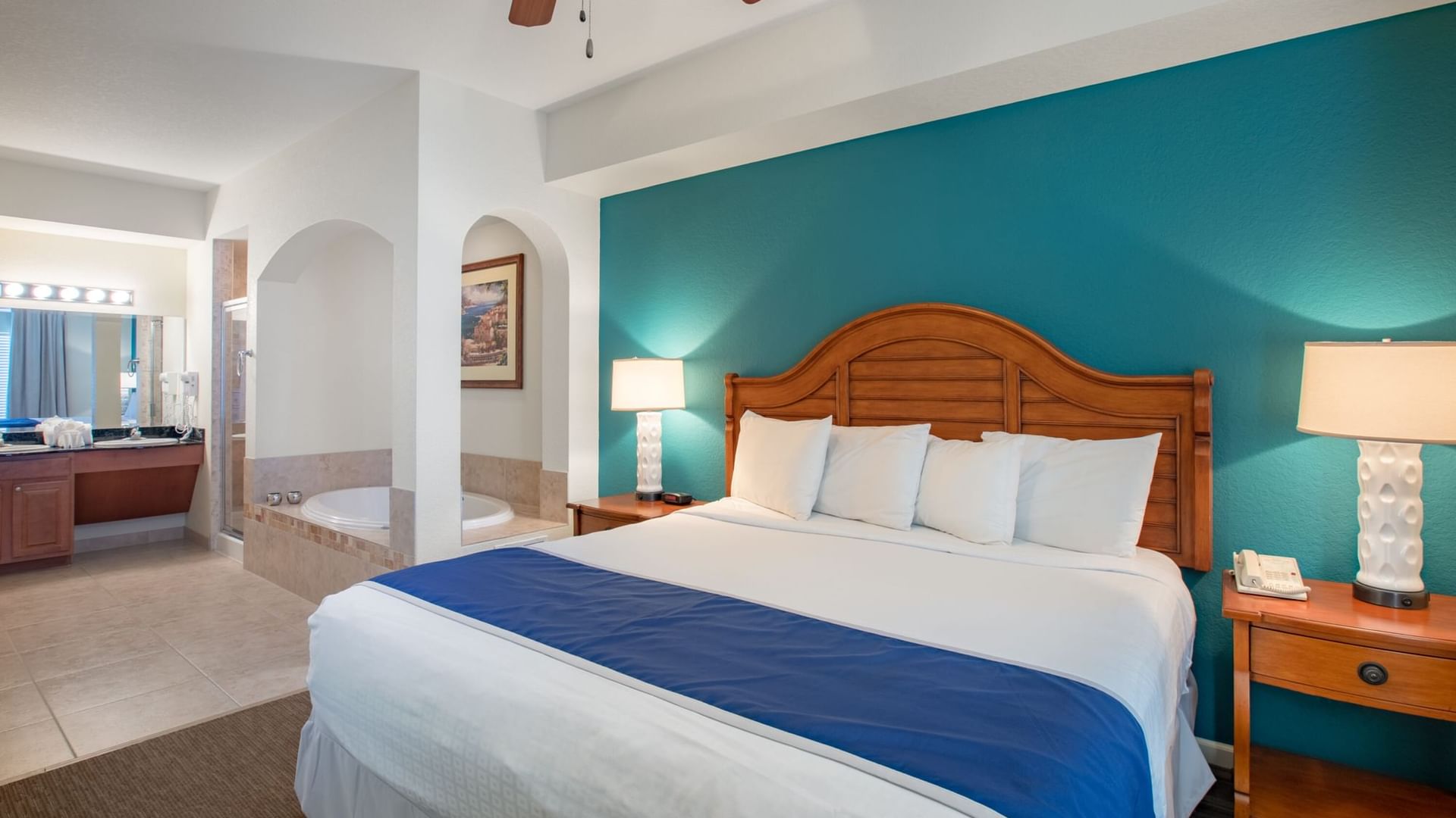 A wide-angle view of a hotel room with a king-sized bed, two nightstands with lamps, and a bathroom with a jacuzzi tub.