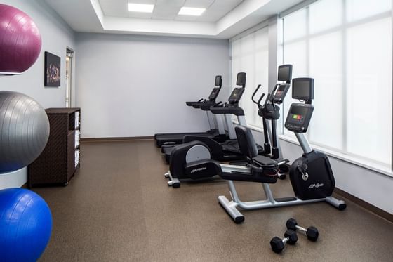 Fitness room with treadmills, bikes, dumbbells, and exercise balls by large bright windows at Star Suites Vero Beach