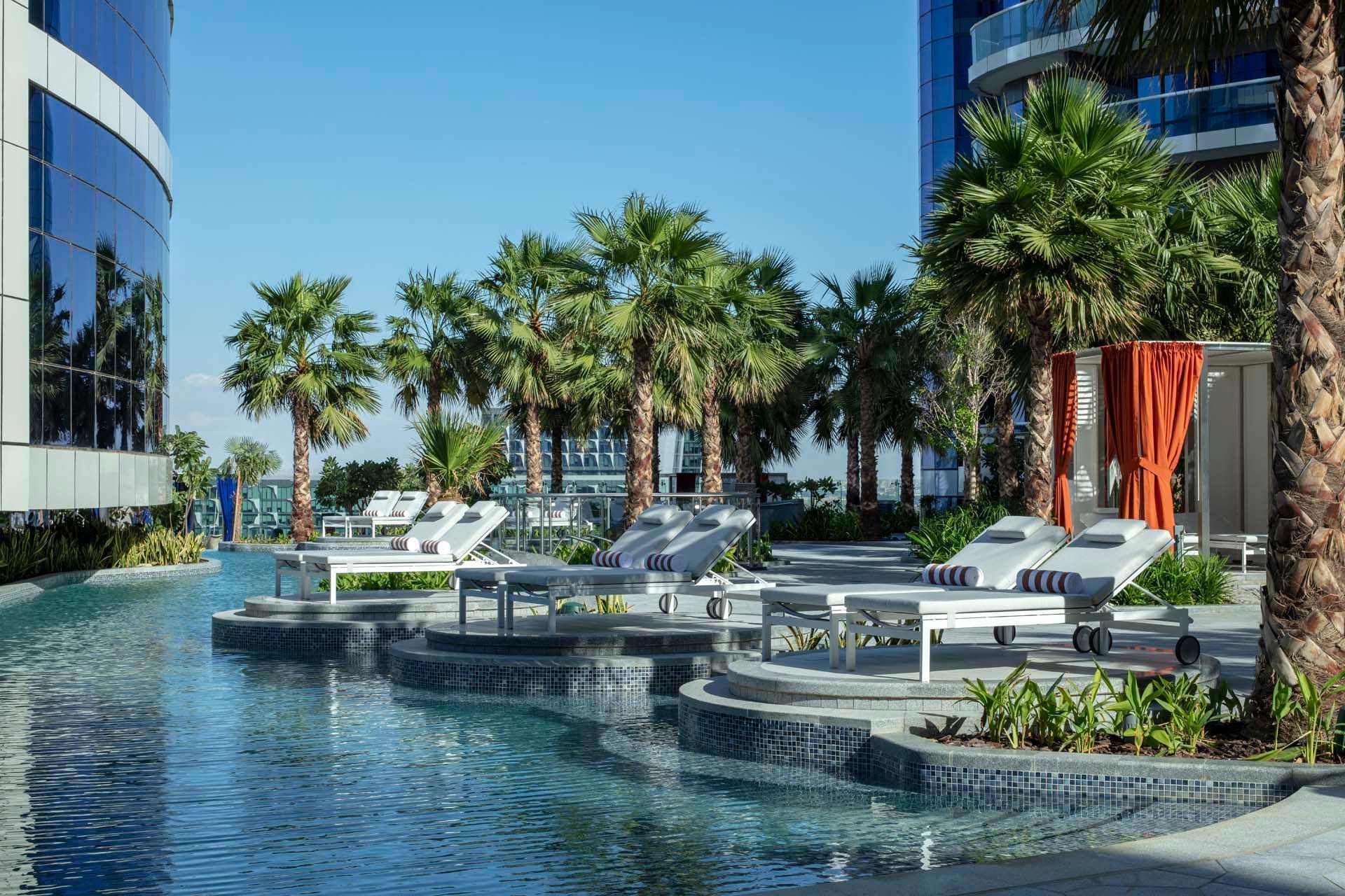 Loungers by the pool deck surrounded by palm trees at Paramount Hotel Dubai