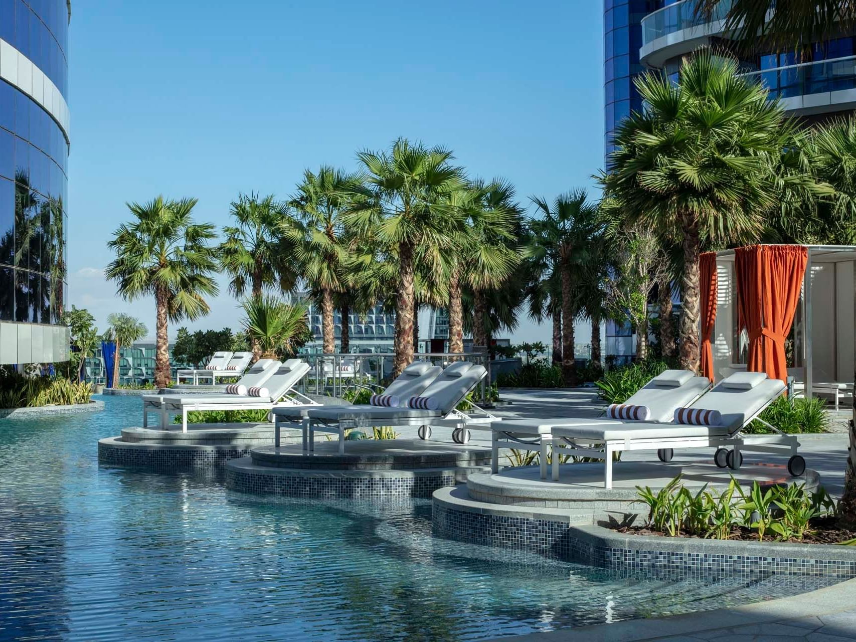 Loungers by the pool deck surrounded by palm trees at Paramount Hotel Dubai