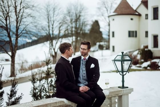 A wedding couple sitting on a bench outside at Schloss Hotel