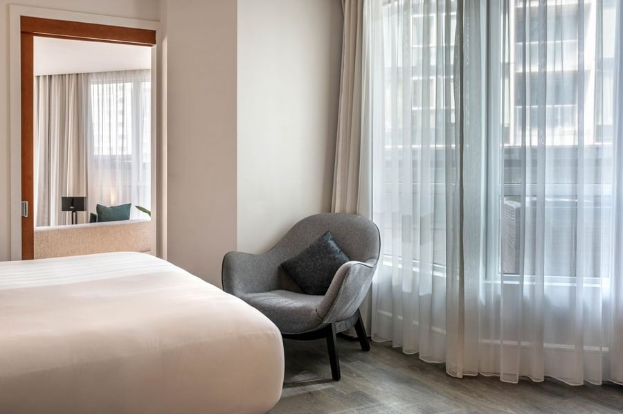 Elegant room with a white bed and a grey chair near the window at Warwick Le Crystal Montreal