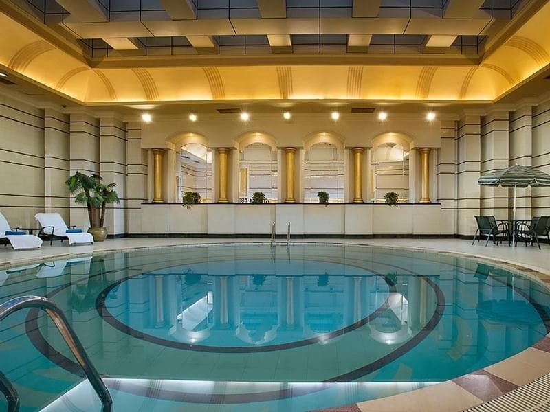 Indoor pool with white loungers and a patio set surrounding the water at Celebrity International Grand Hotel